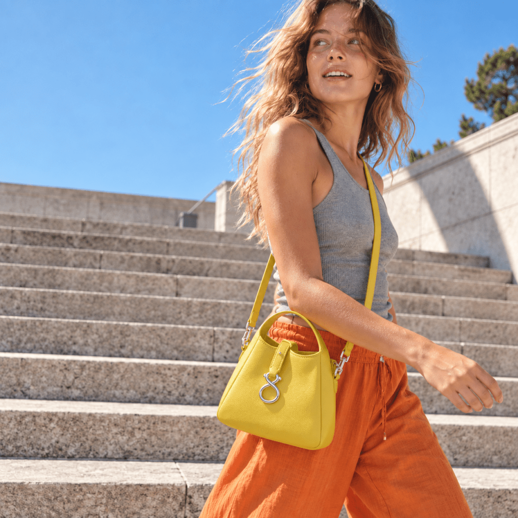 Mujer bajando unas escaleras con un bolso amarillo TOUS en bandolera